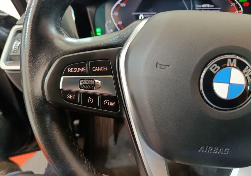 Gros plan sur le volant noir de la BMW Série 3 316d 2022, avec commandes de régulateur et logo central visible.