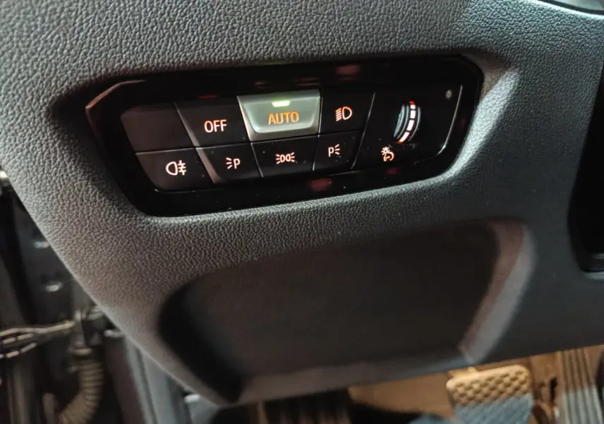 Gros plan sur les commandes d'éclairage à gauche du volant dans l'habitacle gris foncé d'une BMW Série 3 316d 2022.