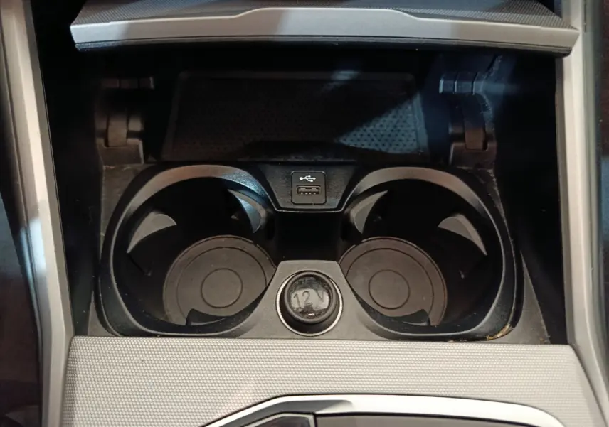 Gros plan sur les porte-gobelets noirs et prise 12V dans la console centrale d'une BMW Série 3 gris clair.