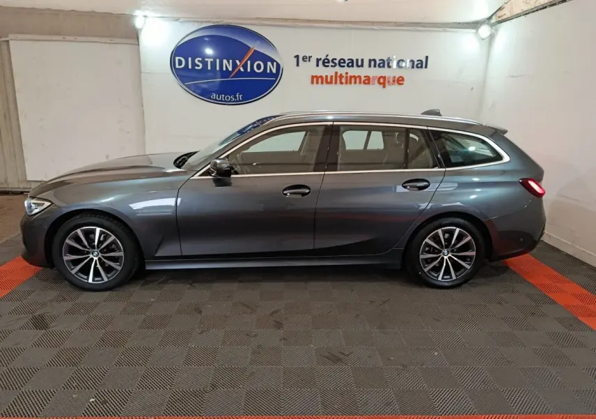 BMW Série 3 Touring gris clair vue de profil côté gauche en intérieur avec jantes alliage et feux arrière allumés