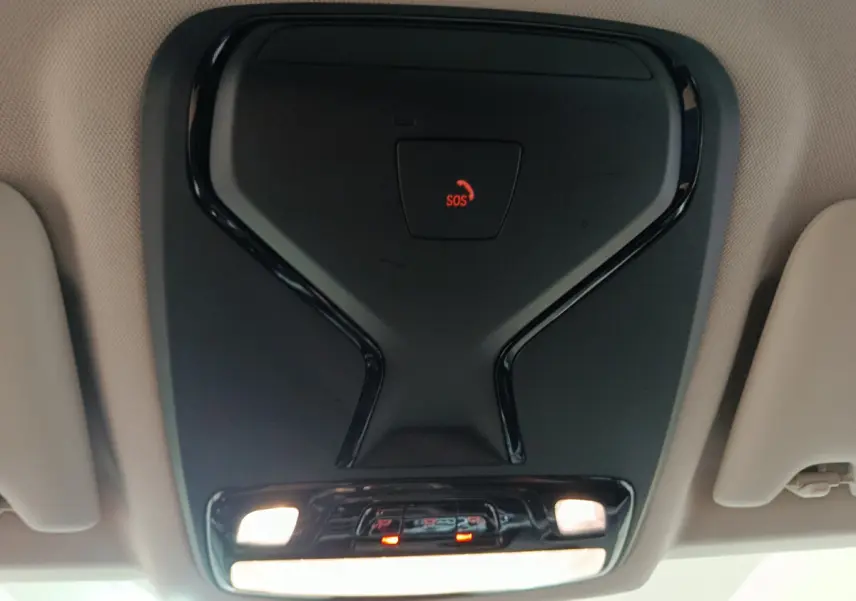 Vue en gros plan du plafonnier noir avec bouton SOS rouge dans l'habitacle beige d'une BMW Série 3 gris clair 2022.