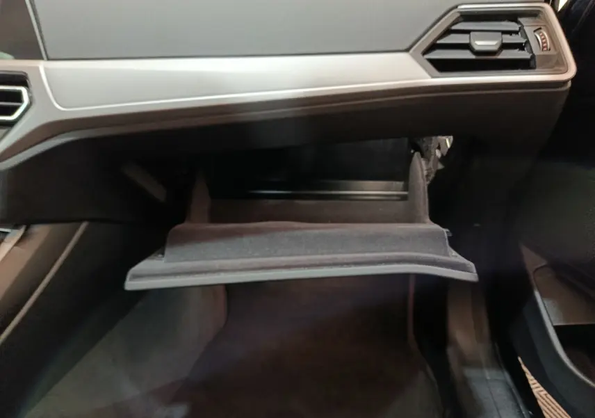 Gros plan sur la boîte à gants ouverte côté passager de la BMW Série 3 316d gris clair, intérieur noir.