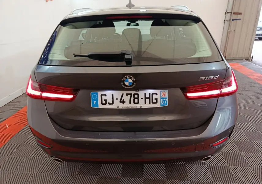 Vue arrière d'une BMW Série 3 316d gris clair avec feux LED allumés et plaque d'immatriculation française visible.