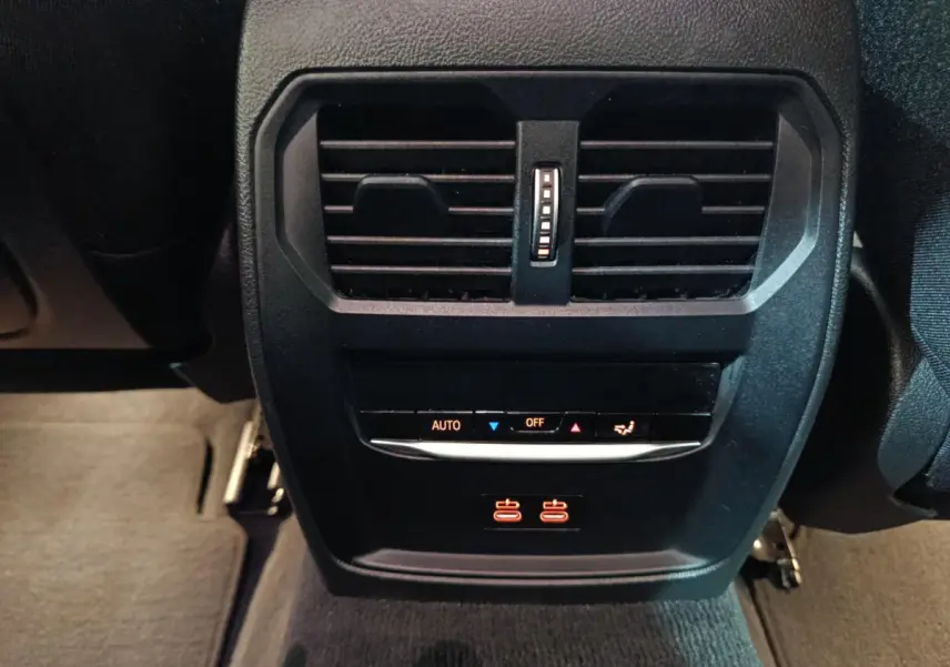 Vue rapprochée des commandes de climatisation arrière et prises USB illuminées dans une BMW Série 3 gris clair 2022.