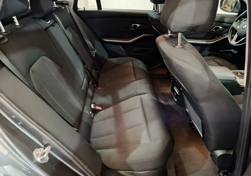 Vue intérieure côté gauche sur la banquette arrière noire et l'avant du tableau de bord d'une BMW Série 3 gris clair 2022.