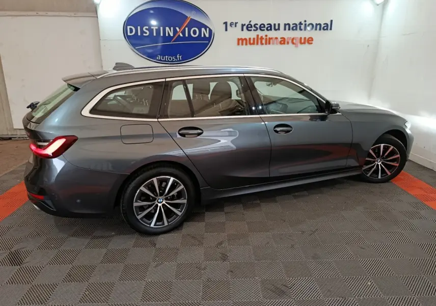 BMW Série 3 316d gris clair vue de profil côté droit, avec feux arrière allumés et jantes alliage distinctives.