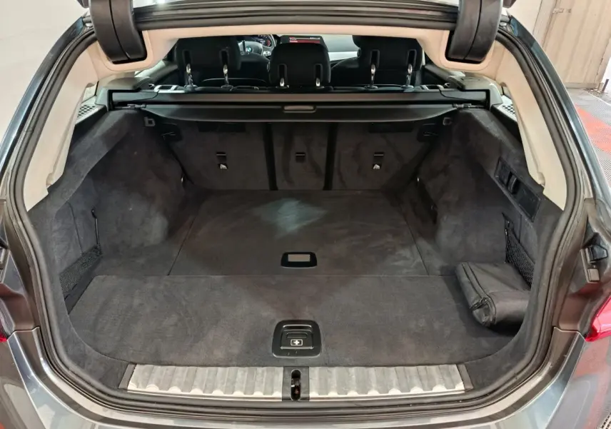 Coffre spacieux ouvert de la BMW Série 3 316d gris clair, vue arrière avec banquette et cache-bagages visibles.