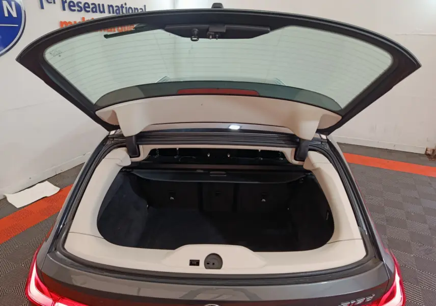 Coffre ouvert vue arrière d'une BMW Série 3 316d gris clair, feux arrière LED allumés dans un garage.