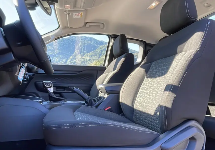 Vue intérieure côté conducteur du Ford Ranger 2025, sièges tissu gris avec accoudoir central et volant cuir multifonctions.