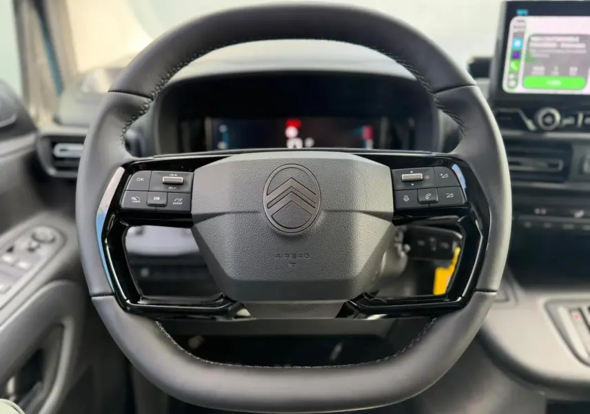 Vue rapprochée du volant cuir multifonctions noir du Citroën Berlingo Multispace 2026, avec tableau de bord numérique en arrière-plan.