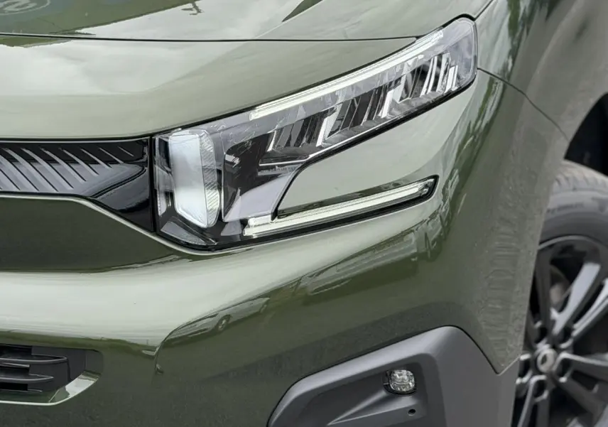 Gros plan sur le phare avant droit du Citroën Berlingo Multispace vert Sirkka avec jante alliage noire visible.