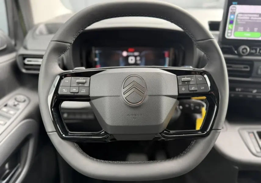 Volant cuir multifonctions Citroën Berlingo Multispace 2026 vu de face, avec commandes intégrées et tableau de bord numérique flou.