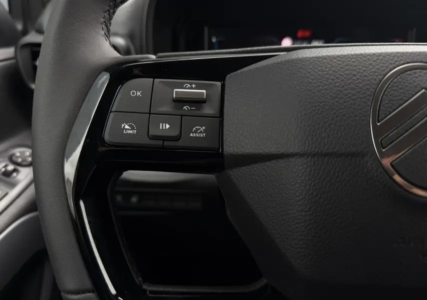 Gros plan sur les commandes gauche du volant cuir noir du Citroën Berlingo Multispace 2026, intérieur sombre.