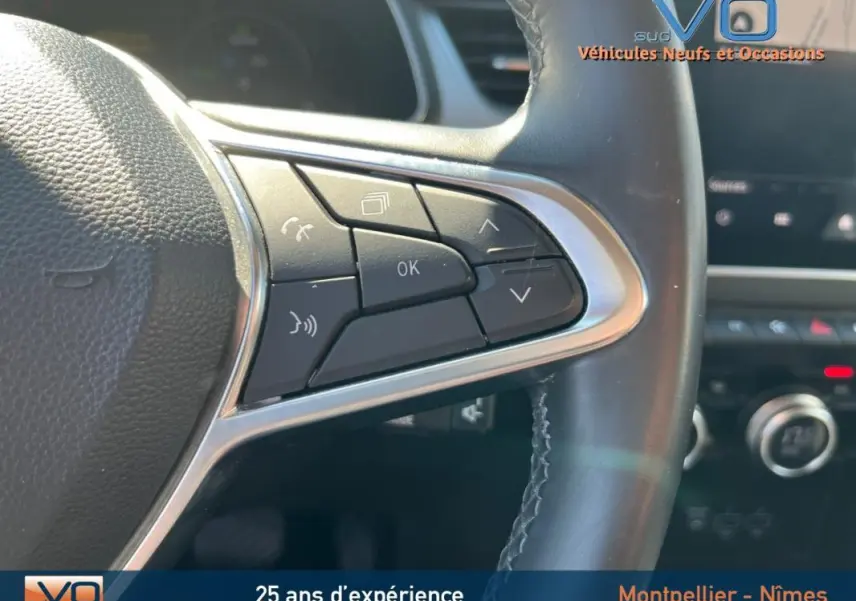 Gros plan sur les commandes au volant cuir du Renault Captur rouge E-Tech Plug-in 160 Intens, tableau de bord en arrière-plan flou.