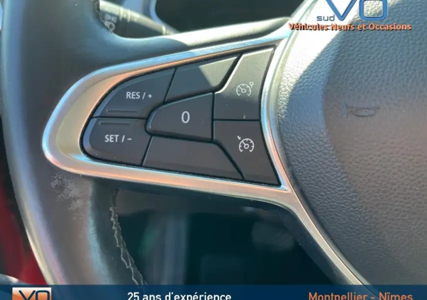 Gros plan sur les commandes du régulateur de vitesse au volant cuir du Renault Captur E-Tech rouge de 2020.