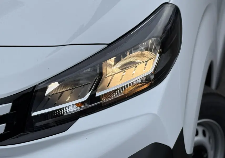 Gros plan sur le phare avant droit du Peugeot Expert Fourgon blanc Icy, avec partie de la roue en arrière-plan.