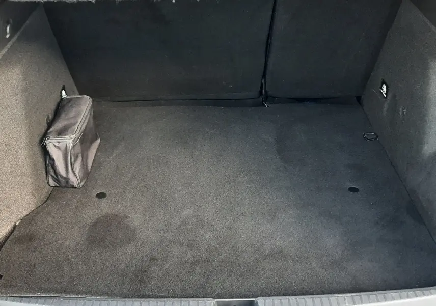 Vue intérieure du coffre spacieux et propre du Dacia Duster bleu 2023, avec une petite trousse noire fixée sur le côté gauche.