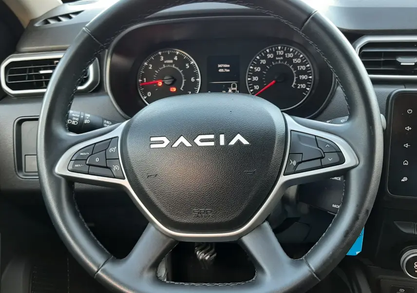 Vue rapprochée du volant noir du Dacia Duster 2023 avec tableau de bord et commandes intégrées visibles.