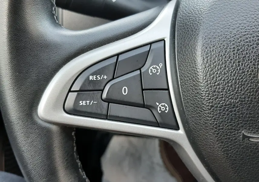 Gros plan sur les commandes de régulateur de vitesse à gauche du volant du Dacia Duster 2023, intérieur noir.