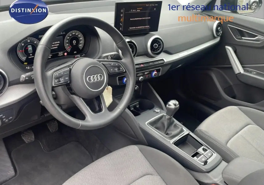 Vue intérieure côté conducteur de l'Audi Q2 30 TDI S-Line 2025, volant cuir, tableau de bord numérique et boîte manuelle.