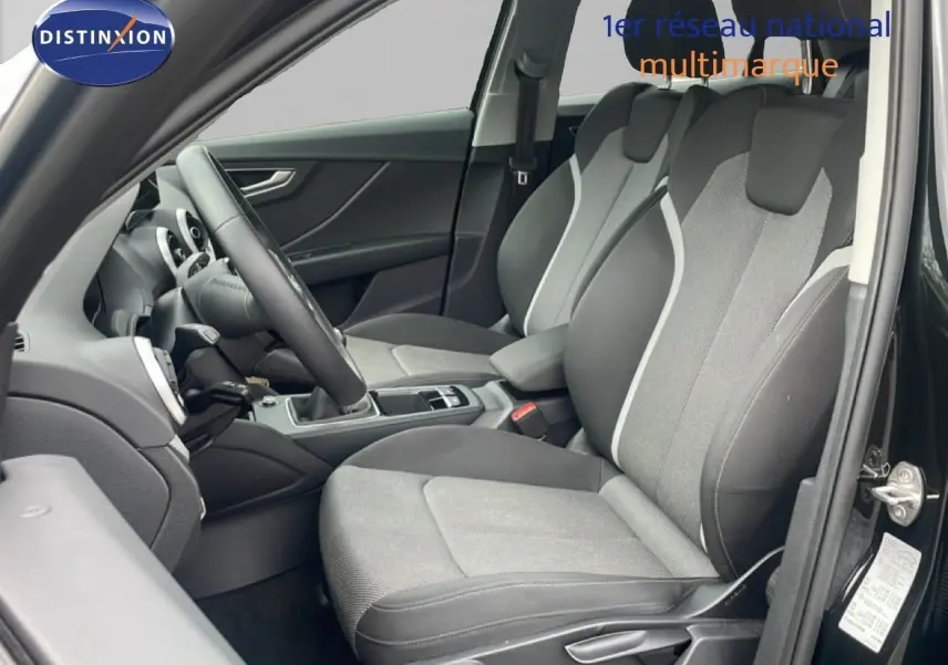 Vue intérieure côté conducteur de l'Audi Q2 30 TDI S-Line 2025 avec sièges tissu gris et noir et volant multifonction.