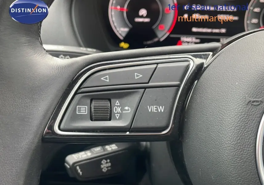 Gros plan sur les commandes au volant noir de l'Audi Q2 30 TDI S-Line 2025 avec tableau de bord numérique en arrière-plan flou.