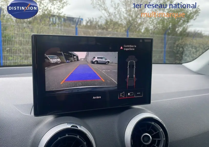 Écran central affichant la caméra de recul d’un Audi Q2 noir mito metal, avec guidage de trajectoire en bleu et orange.