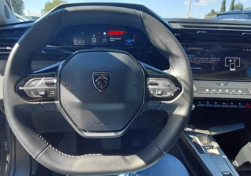 Vue intérieure centrée sur le volant cuir noir et le cockpit numérique de la Peugeot 308 gris 2025.