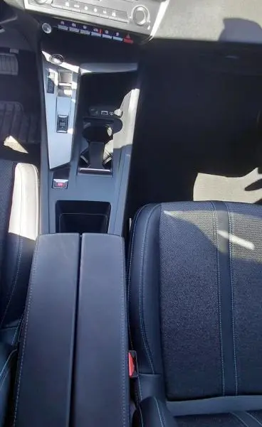 Vue plongeante sur la console centrale noire et l'accoudoir du Peugeot 308 gris, avec levier de boîte automatique et sièges en tissu.