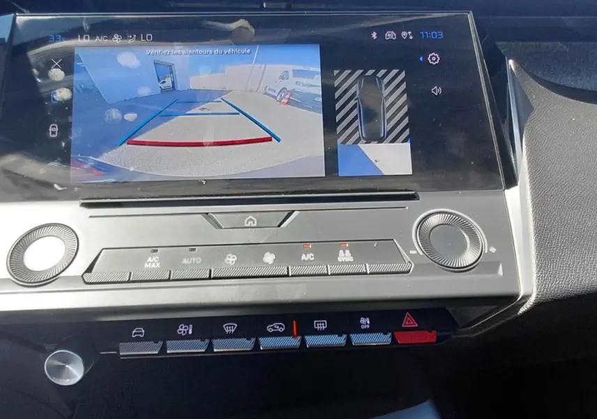 Vue rapprochée de l'écran central de la Peugeot 308 gris 2025 affichant la caméra de recul et les commandes climatisation.