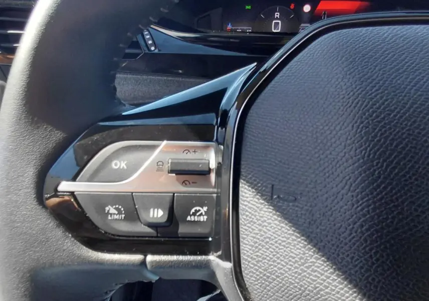 Gros plan sur le volant gris du Peugeot 308 2025, avec commandes intégrées et logo lion visible.