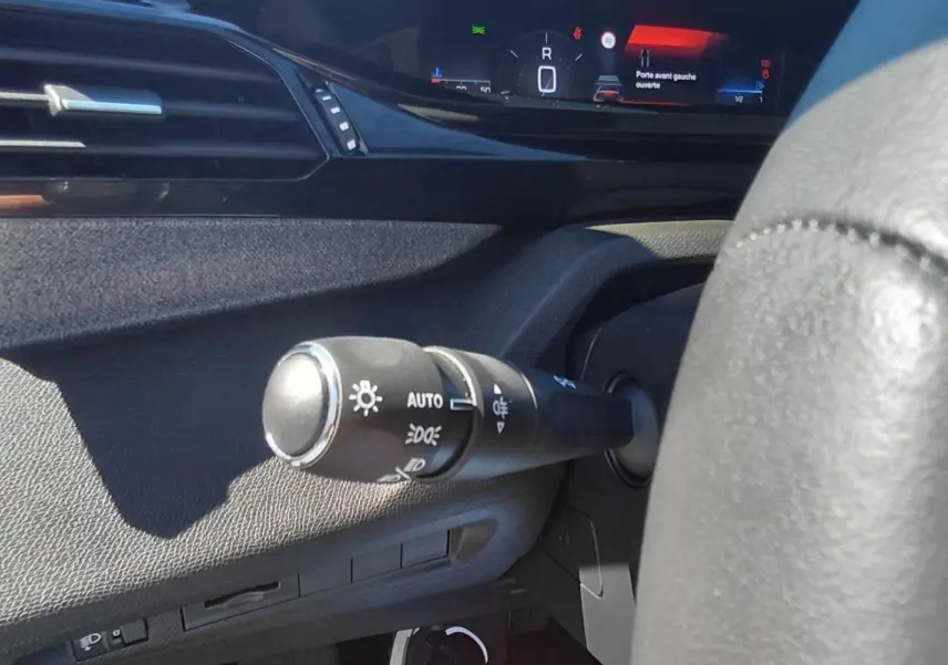 Gros plan sur la commande des feux à gauche du volant dans l’habitacle gris du Peugeot 308 2025, affichage numérique visible.