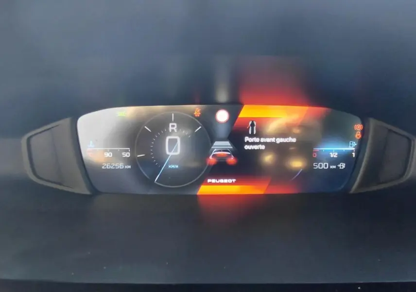 Vue rapprochée du cockpit numérique de la Peugeot 308 gris, affichant la vitesse, l'alerte porte avant gauche ouverte et l'autonomie.
