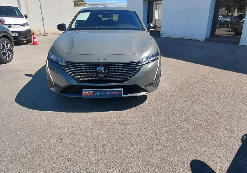 Vue de face d'une Peugeot 308 gris métallisé 2025 avec calandre distinctive et phares fins, stationnée en extérieur.