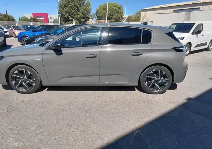 Vue de profil côté gauche d'une Peugeot 308 gris métallisé garée en extérieur sur un parking.