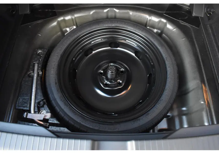 Vue plongeante sur la roue de secours noire à encombrement réduit dans le coffre d’un Volkswagen T-Roc Grenadilla Black.