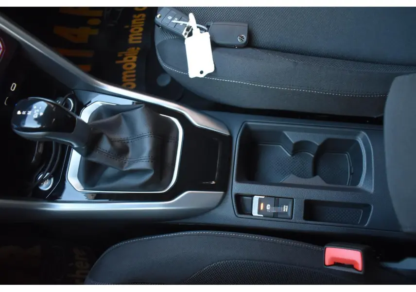 Vue intérieure en plongée sur la console centrale du Volkswagen T-Roc noir, avec levier de boîte automatique et porte-gobelets.