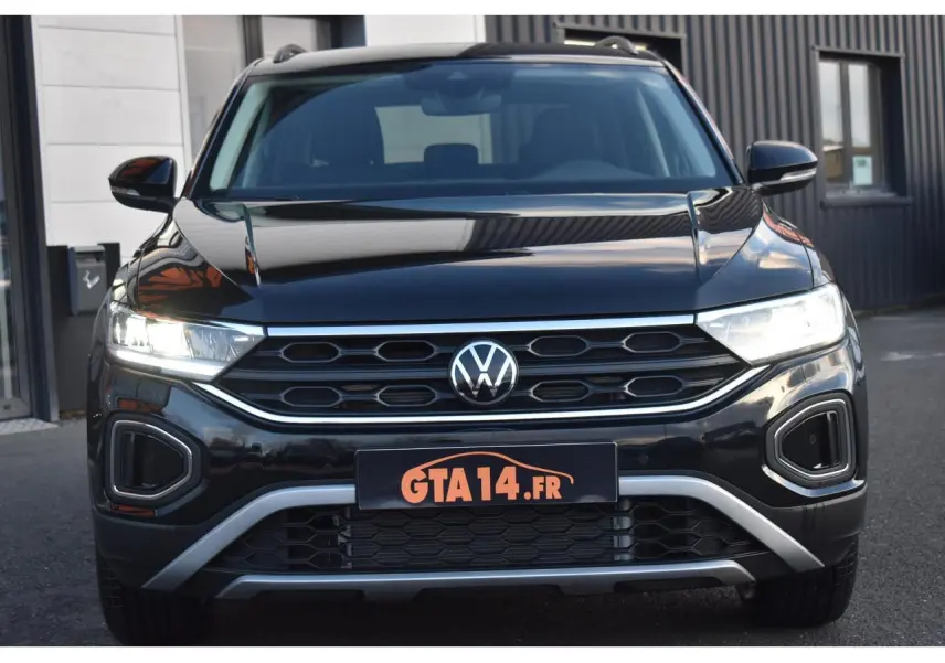 Vue de face du Volkswagen T-Roc 2025 noir Grenadilla avec calandre hexagonale et feux LED allumés.