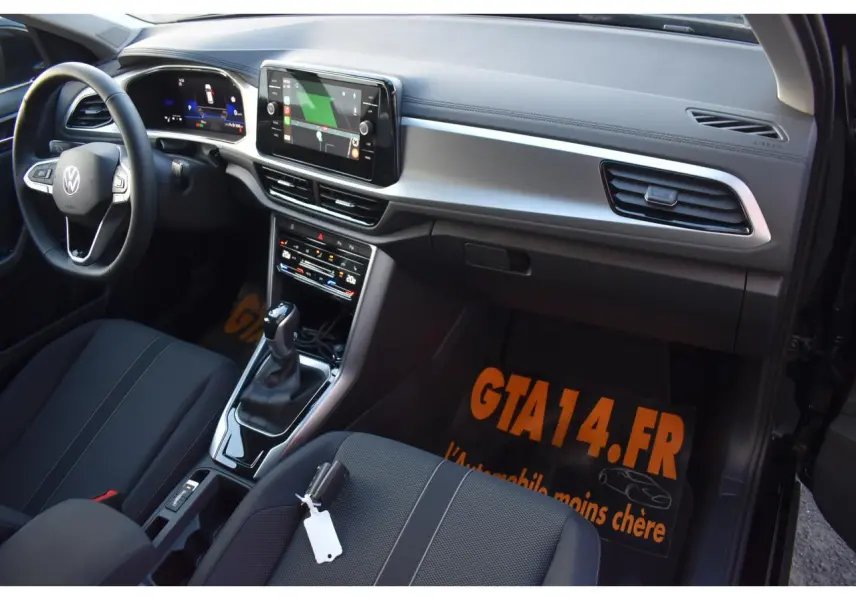 Vue intérieure côté passager avant du Volkswagen T-Roc 2025, sellerie tissu noir et console centrale avec écran tactile.