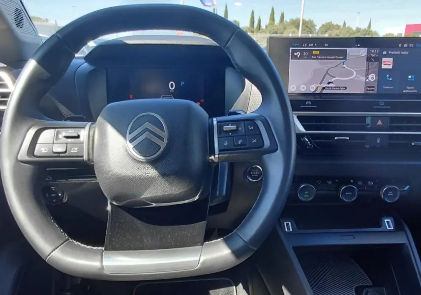 Vue intérieure centrée sur le volant cuir et le tableau de bord numérique du Citroën C4 X noir 2025 hybride.