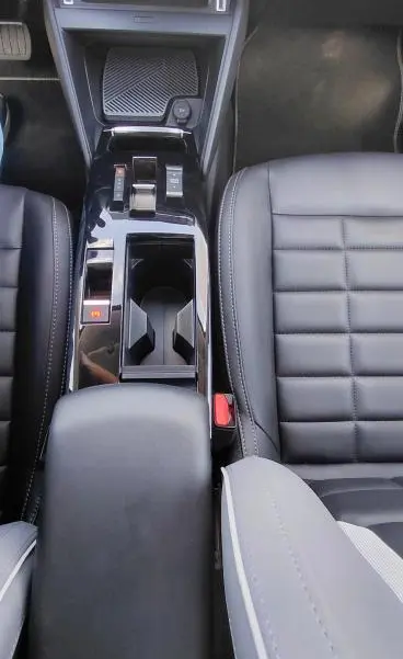 Vue plongeante sur la console centrale noire et les sièges en cuir du Citroën C4 X Hybride 2025, avec accoudoir central.