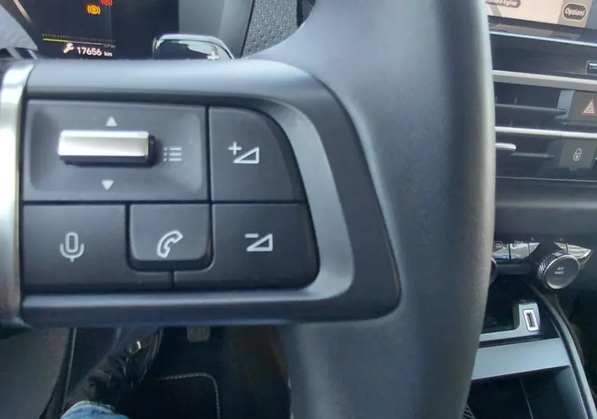 Gros plan sur les commandes gauche du volant cuir de la Citroën C4 X noire, avec tableau de bord et console en arrière-plan.