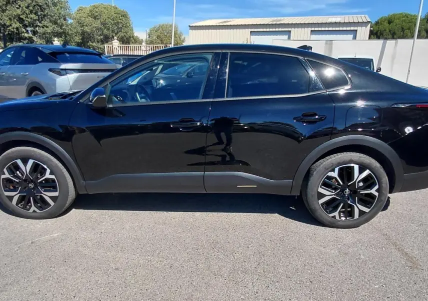 Profil côté gauche d'une Citroën C4 X hybride noire 2025 avec jantes alliage 17 pouces et toit ouvrant panoramique.