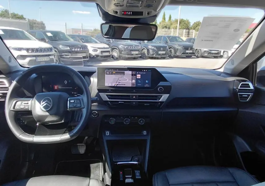 Vue intérieure avant du Citroën C4 X noir 2025, montrant le tableau de bord moderne et le volant cuir avec commandes intégrées.