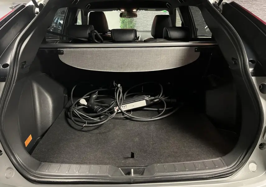 Coffre ouvert d'un Mitsubishi Eclipse Cross gris avec câble de recharge hybride visible et cache-bagages déployé.