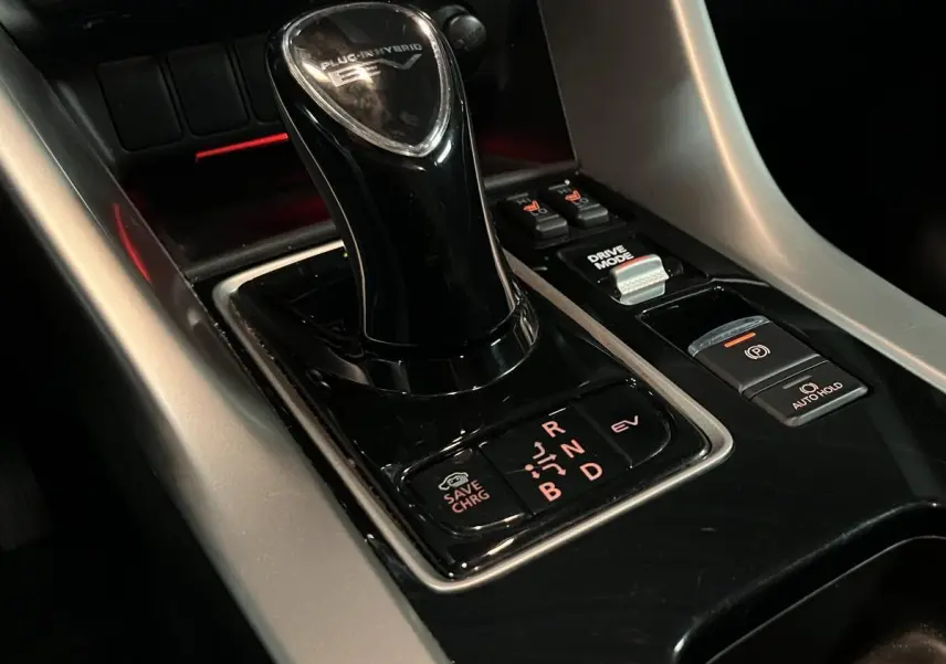 Gros plan sur le levier de vitesse noir brillant du Mitsubishi Eclipse Cross hybride rechargeable, avec commandes autour.