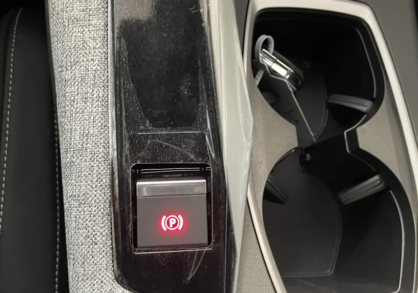 Gros plan sur la console centrale du Peugeot 3008 blanc, avec bouton de frein à main électronique allumé et porte-gobelets noirs.