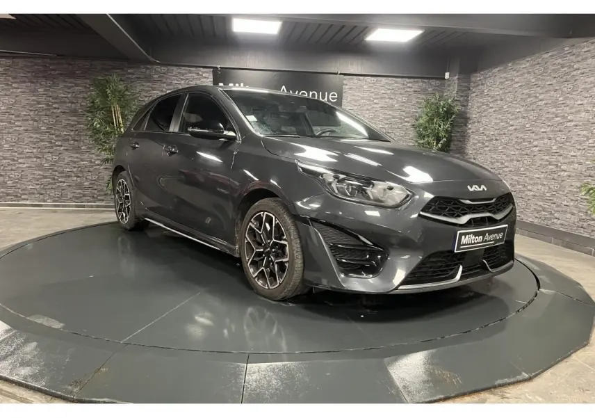 Kia Ceed gris métallisé vue 3/4 avant droit avec jantes alliage et calandre noire laquée dans showroom.
