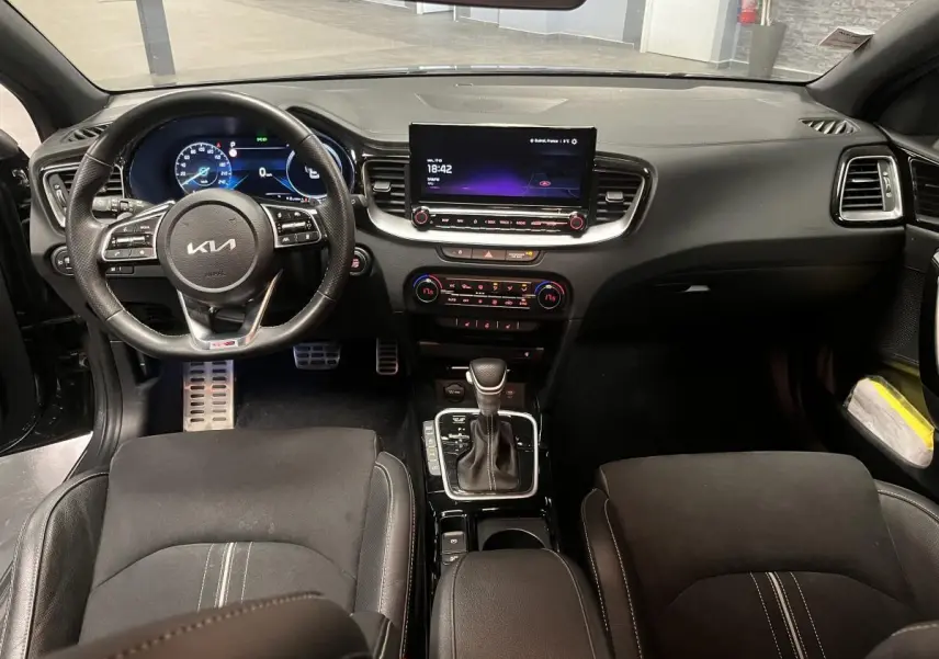 Vue intérieure avant de la Kia Ceed 2023 gris, tableau de bord moderne avec écran tactile et volant cuir multifonction.
