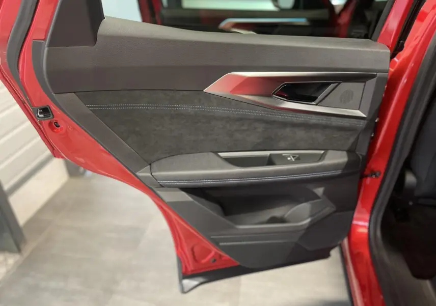 Vue rapprochée de la porte arrière gauche rouge métallisé du Renault Austral avec garniture noire et surpiqûres blanches.